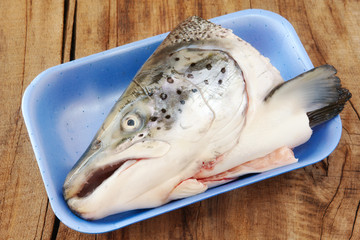 Raw salmon head in polystyrene food box on wooden table