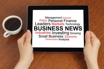 Hands hold tablet PC with tag cloud of business news