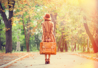 Redhead girl with suitcase in the autumn park.