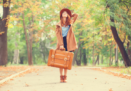 Redhead girl with suitcase in the autumn park.