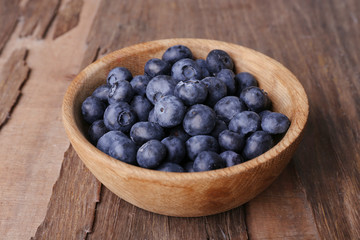 Wooden bowl of blueberries on wooden background closeup