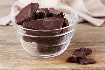 Cracked chocolate bar in glass bowl, on wooden background