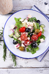 Plate of Greek salad served on napkin on wooden background