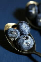 Tasty ripe blueberries in spoons, on wooden background