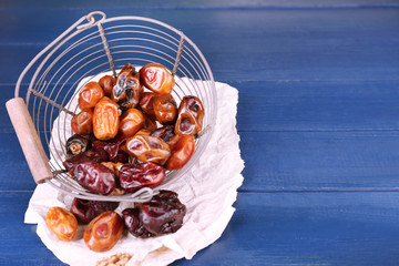 Tasty dates fruits in metal basket, on blue wooden table