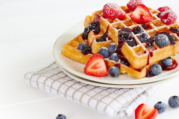Golden waffles with berries on white table