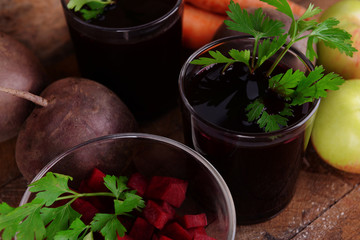 Glasses of fresh beet juice and vegetables on wooden background