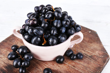 Purple grapes in bowl on wooden background