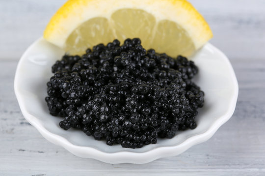 Black caviar with lemon on plate on grey wooden background