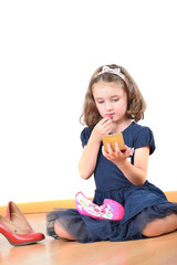 Little cute girl putting on lipstick in the mirror