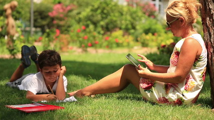 mother using digital tablet and son drawing pictures in the park