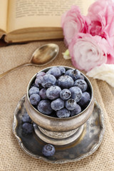 Silver bowl of blueberries, pink eustoma flowers in the backgrou