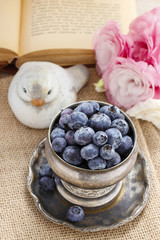 Silver bowl of blueberries, pink eustoma flowers in the backgrou