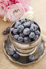 Silver bowl of blueberries, pink eustoma flowers in the backgrou