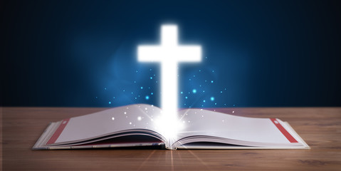 Open holy bible with glowing cross in the middle