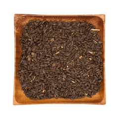 Black sunflower seeds in a wooden bowl on a white background