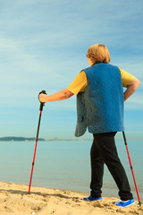 active woman senior nordic walking on a beach. from behind