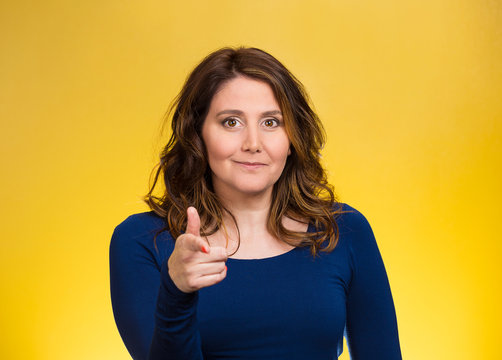 Woman smiling pointing finger towards you yellow background 