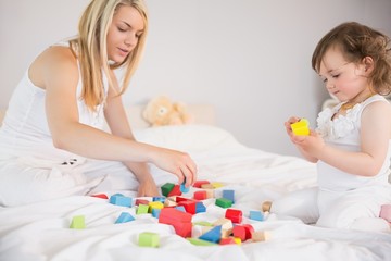 Mother and daughter playing with building blocks on bed