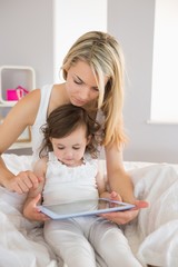 Mother and daughter using digital tablet on bed