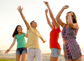 smiling friends dancing on summer beach