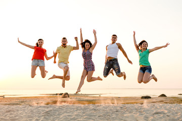 smiling friends dancing and jumping on beach
