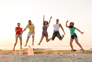 smiling friends dancing and jumping on beach