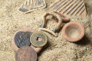 Fototapeta na wymiar pezzi di vasi antichi su sabbia con monete antiche