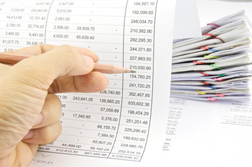 Man auditing account by pencil with pile of paperwork
