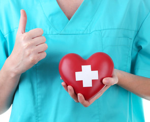 Red heart with cross sign in doctor hand, close-up, isolated
