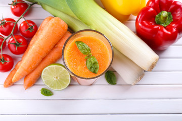 Glass of fresh carrot juice and vegetables on wooden background