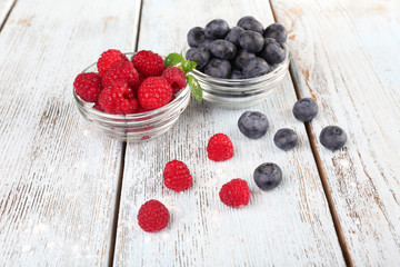 Glass bowls of raspberries and blueberries on wooden background