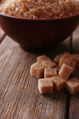 Brown sugar cubes and crystal sugar in bowl on wooden