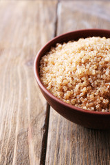 Brown crystal sugar in bowl on wooden background