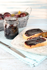 Bread with plum jam and plums on wooden table