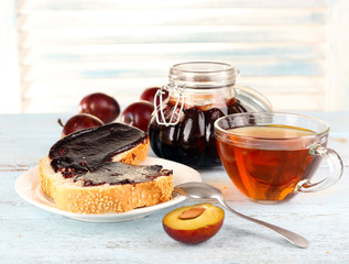 Bread with plum jam and tea on wooden table