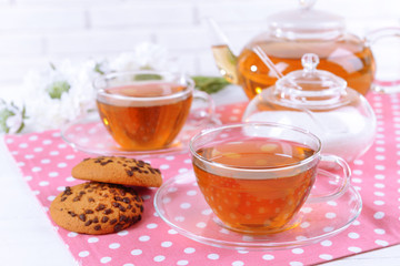Teapot and cups of tea on table on brick wall background