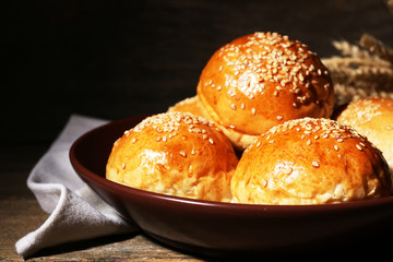 Tasty buns with sesame on plate, on wooden background