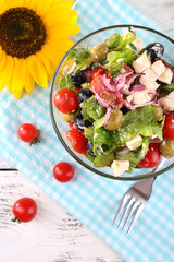 Glass bowl of Greek salad served on napkin on wooden background