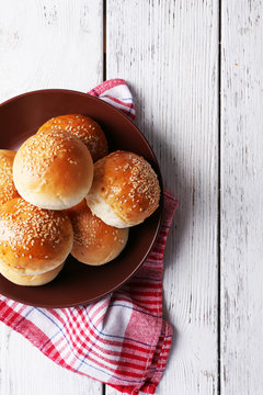 Tasty buns with sesame on plate, on color wooden background