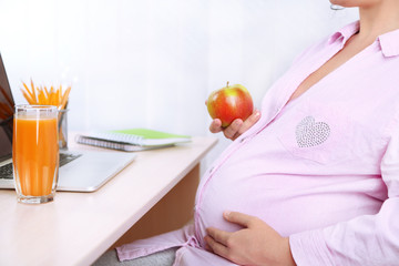 Young pregnant woman holding apple in office