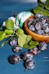 Ripe sweet plums in bowl, on wooden table