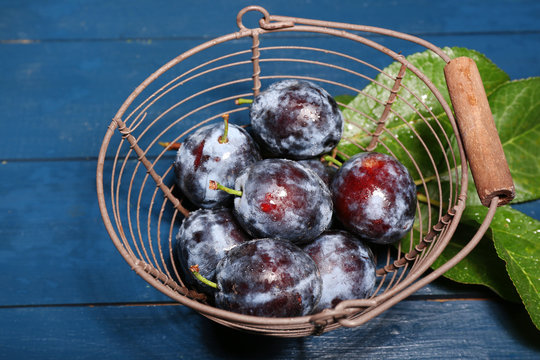 Ripe sweet plums in metal basket, on wooden table