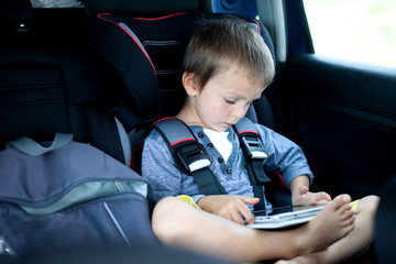 Cute boy, playing on tablet in the car