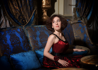 Fototapeta premium Woman in cocktail dress sitting on sofa in luxury interior