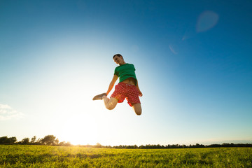 Young man jumping on meadow with dandelions