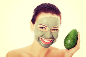 Beautiful woman with facial mask holding avocado.