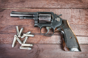 black revolver gun with bullets isolated on wooden background © Delicious