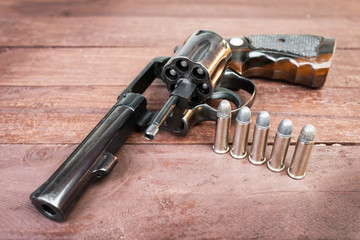 black revolver gun with bullets isolated on wooden background © Delicious