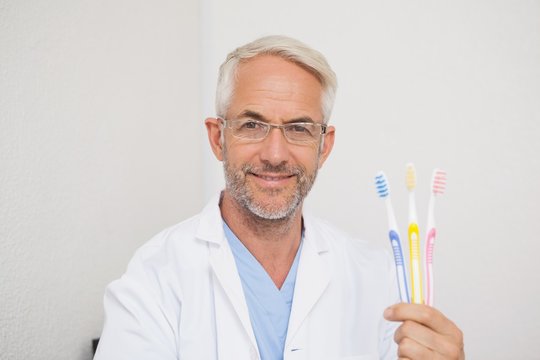 Dentist smiling at camera holding toothbrushes